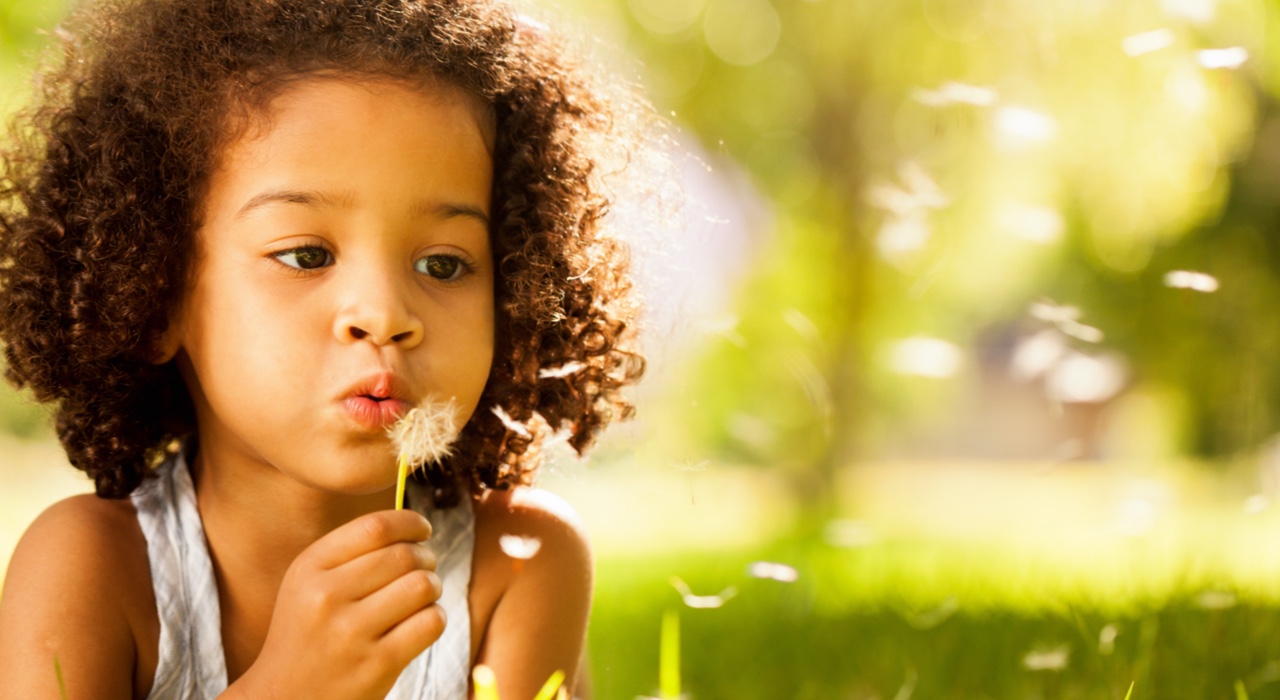 Photo of a young girl blowing seeds off a dandelion.